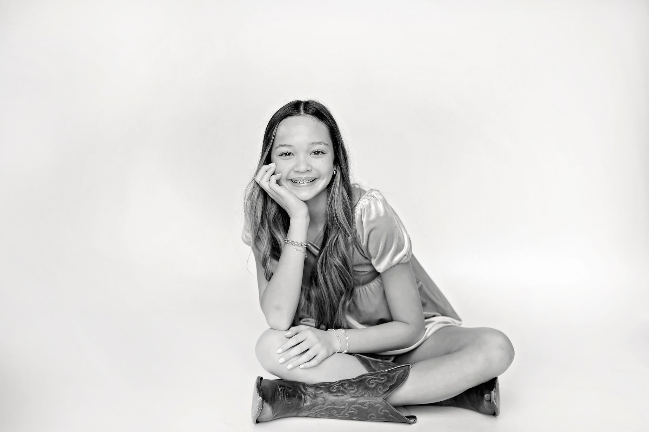 Black and white portrait of person sitting cross-legged with hand on face and casual pose.