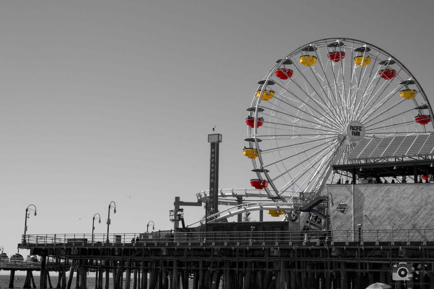 A Ferris wheel with selective color highlighting against a black and white pier backdrop.
