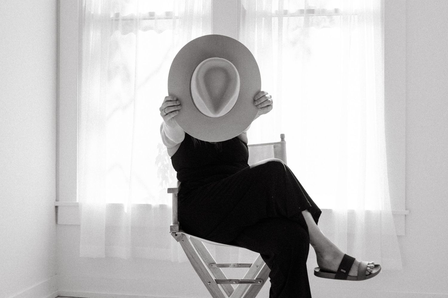 A artistic black and white portrait of someone posing with a hat on a chair.