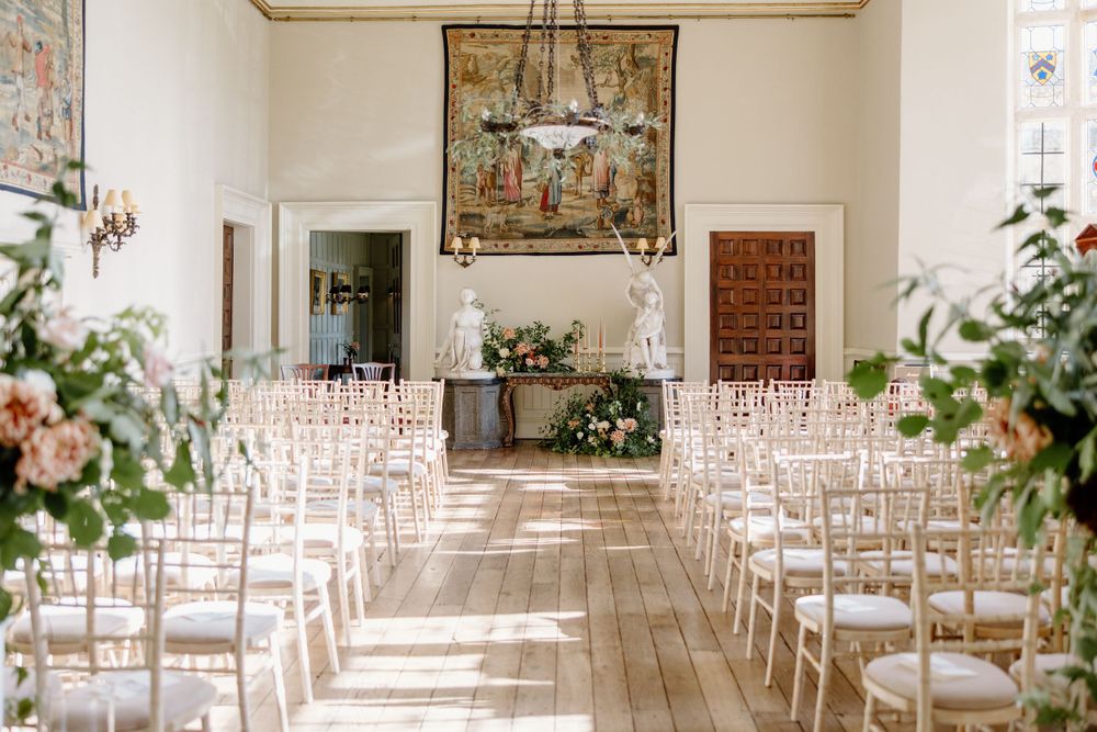 Elegant wedding ceremony space with white chairs, floral arrangements and natural light streaming in.