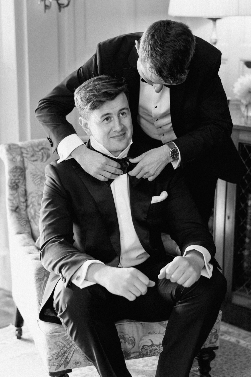 Black and white photo of two people adjusting formal attire before event.