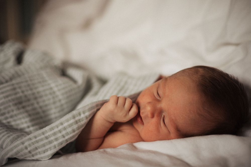 A peaceful sleeping newborn with hand raised to face rests on white bedding.