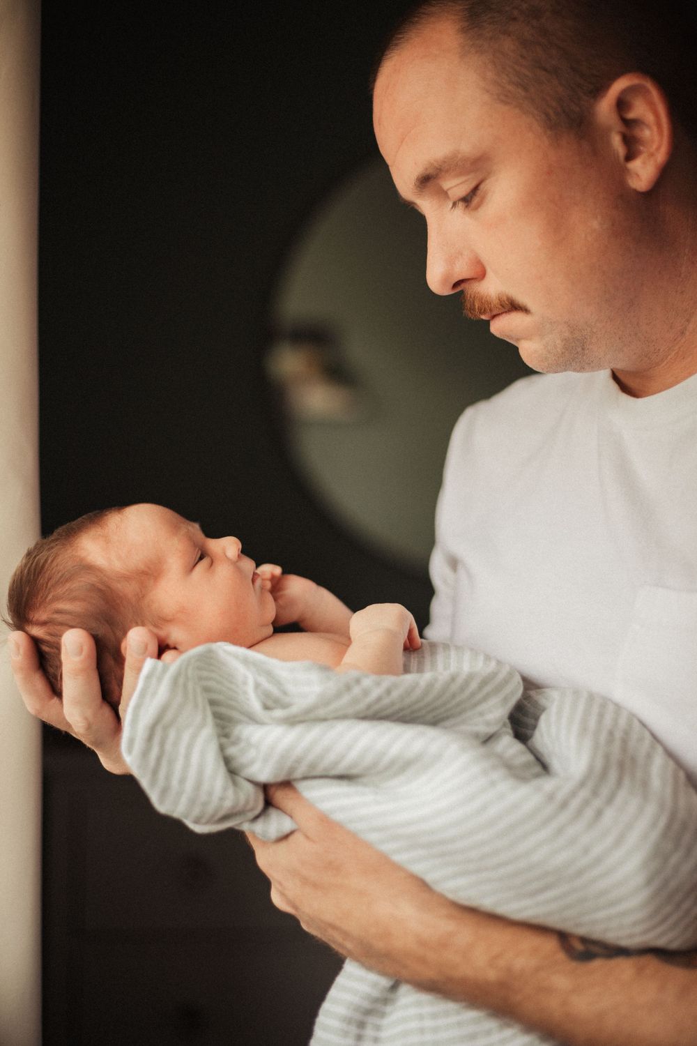 A tender moment between parent and newborn swaddled in a striped blanket.
