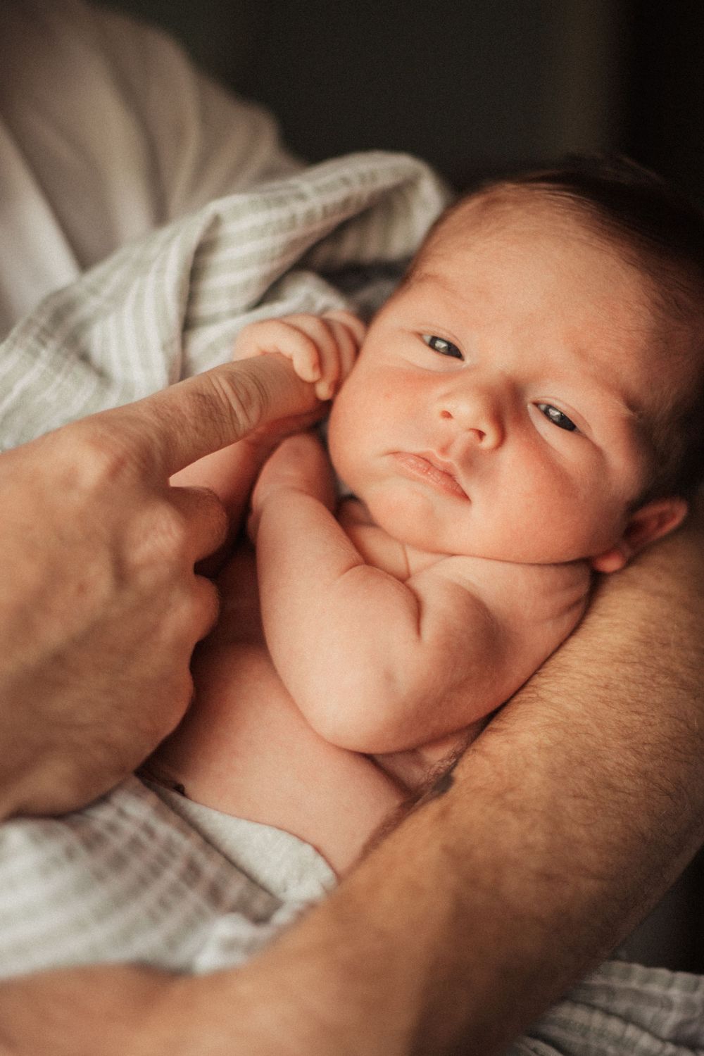 A newborn with bright alert eyes looking at camera while being held.