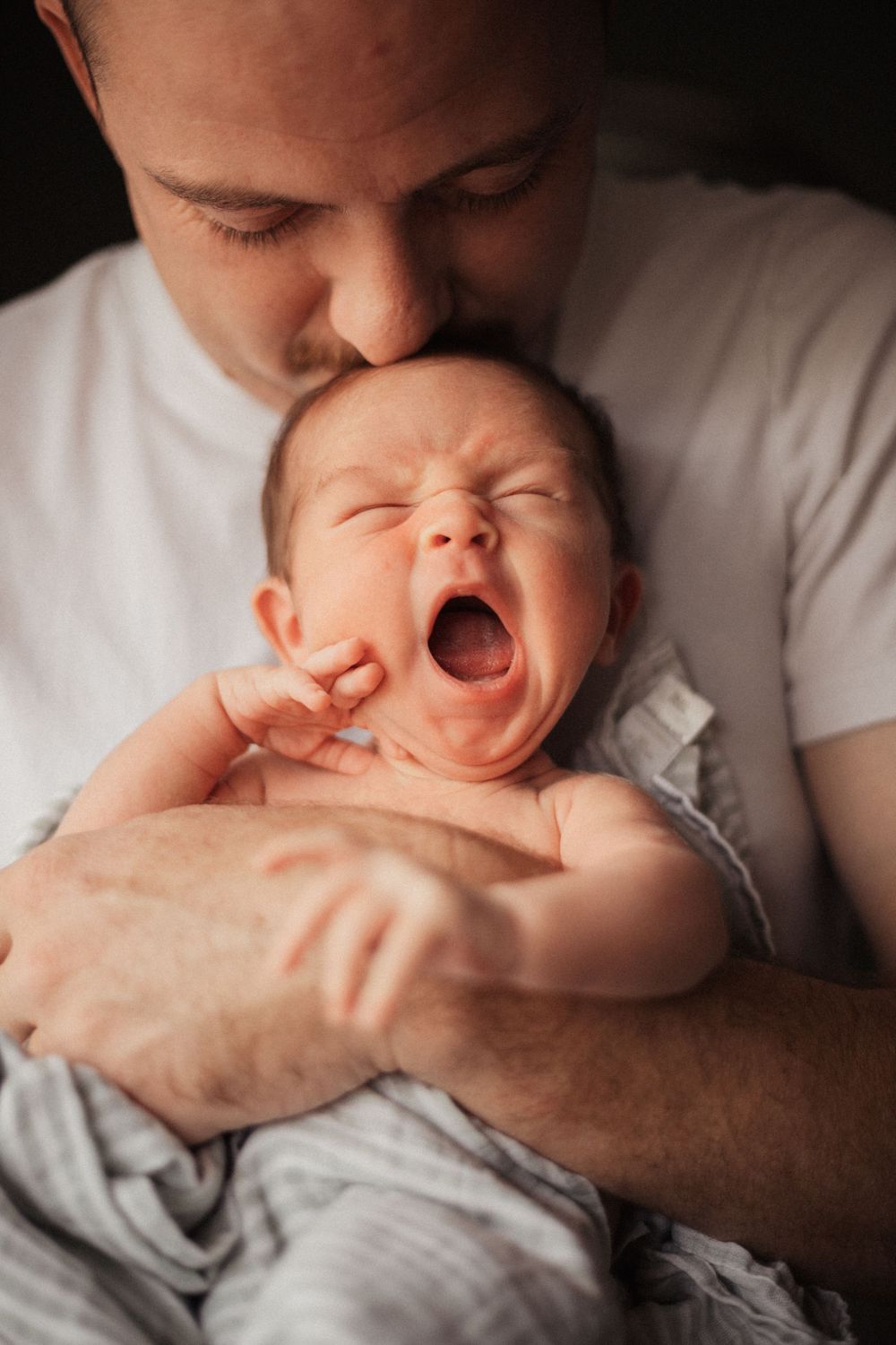 A yawning newborn being held against parent's chest in intimate portrait.