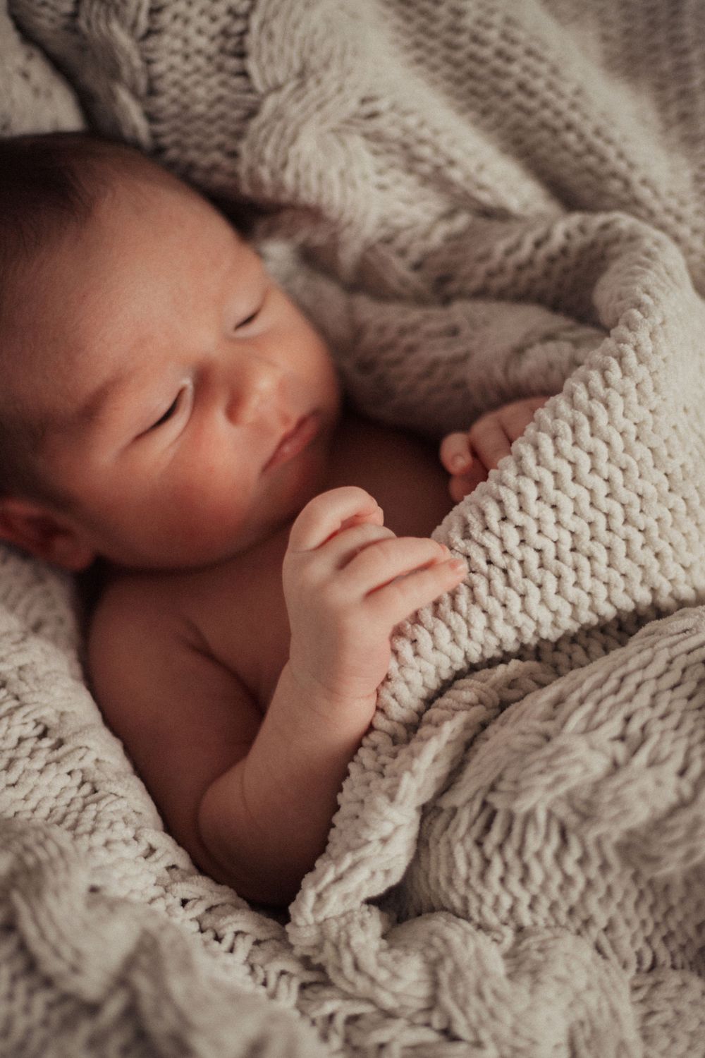 A sleeping newborn nestled in cozy knitted blanket with soft natural lighting.