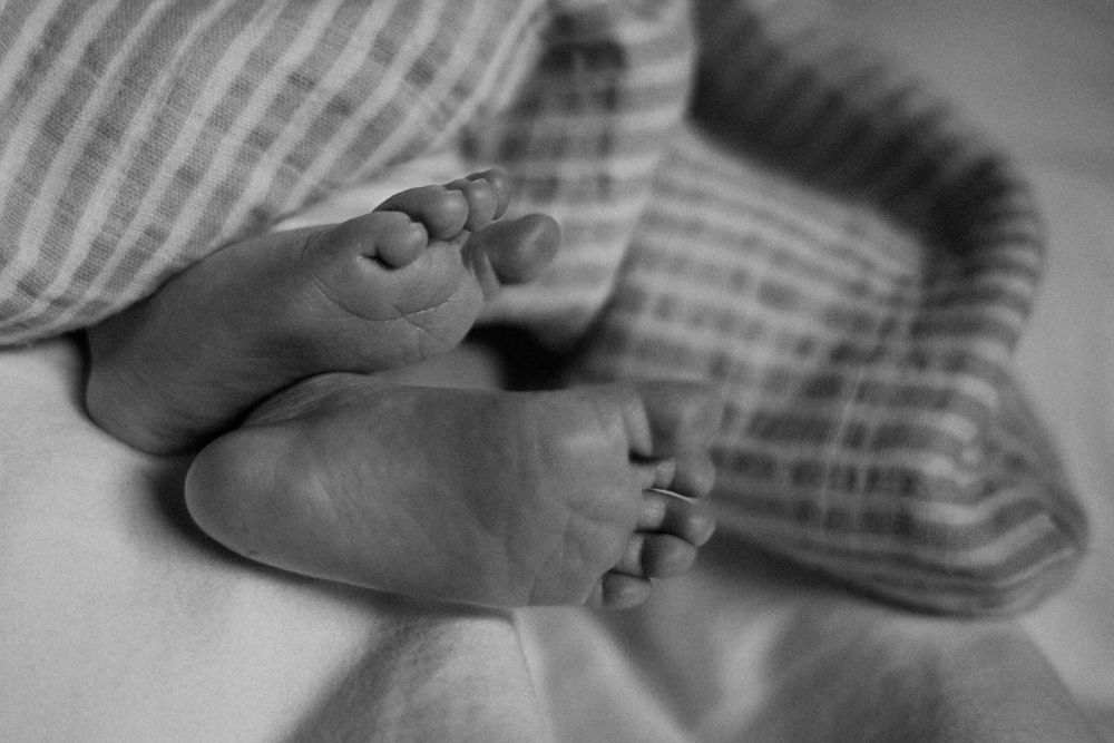 Close-up black and white photo of newborn feet against striped fabric.