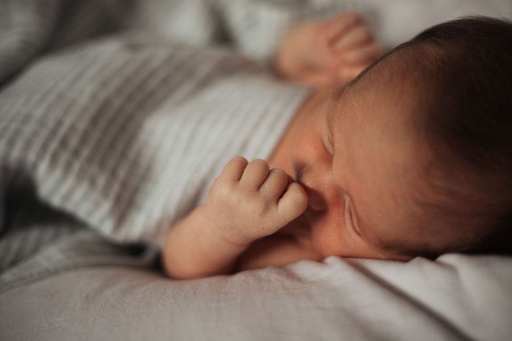 A sleeping newborn with tiny fingers curled up against their face on light bedding.