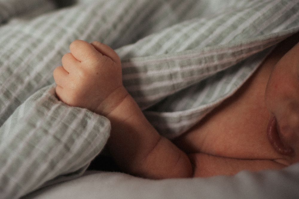 A tiny newborn's foot peeks out from under a soft striped blanket while resting.