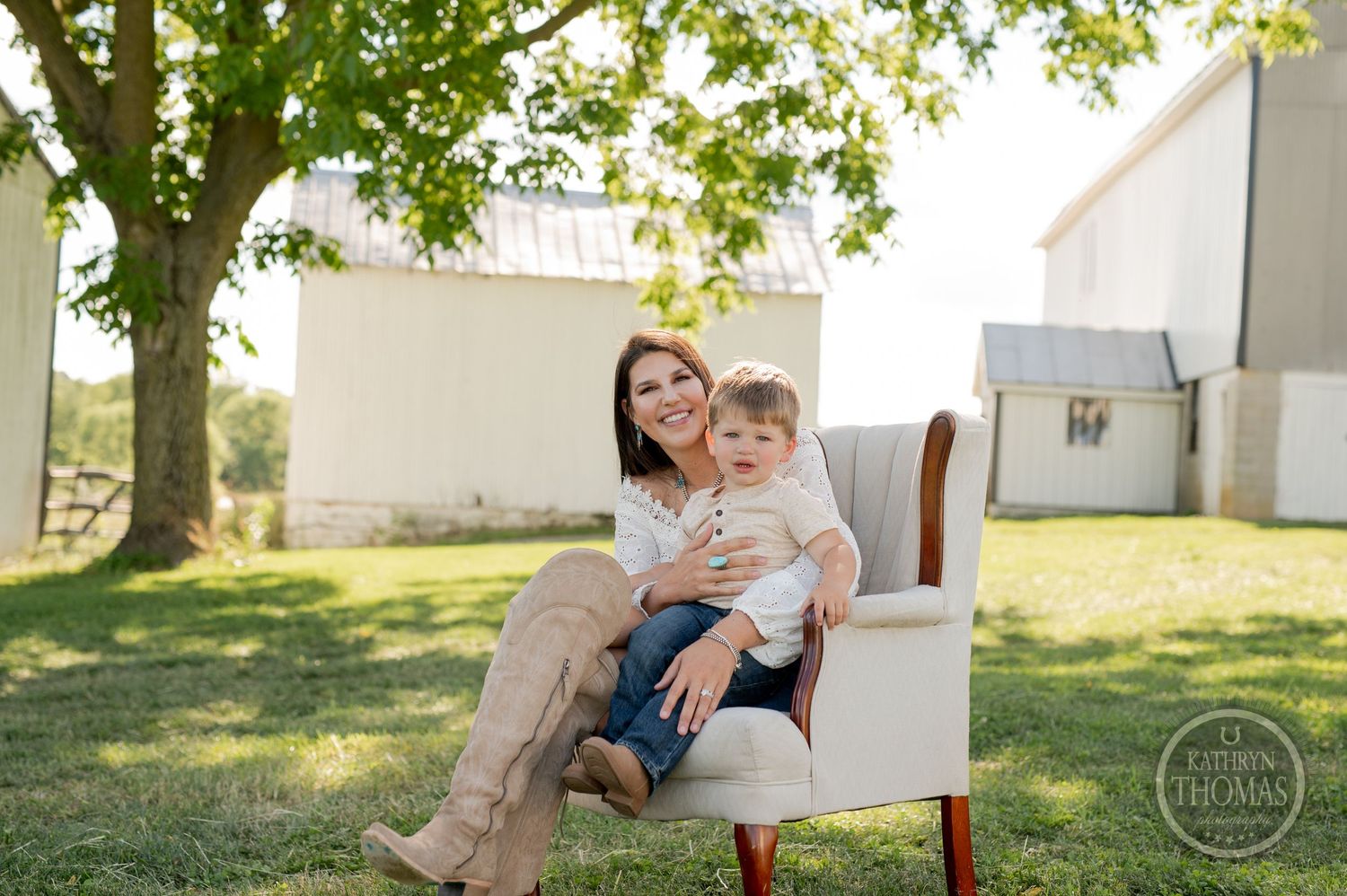 A parent and young child share a tender moment together in a white upholstered chair outdoors on a sunny day.