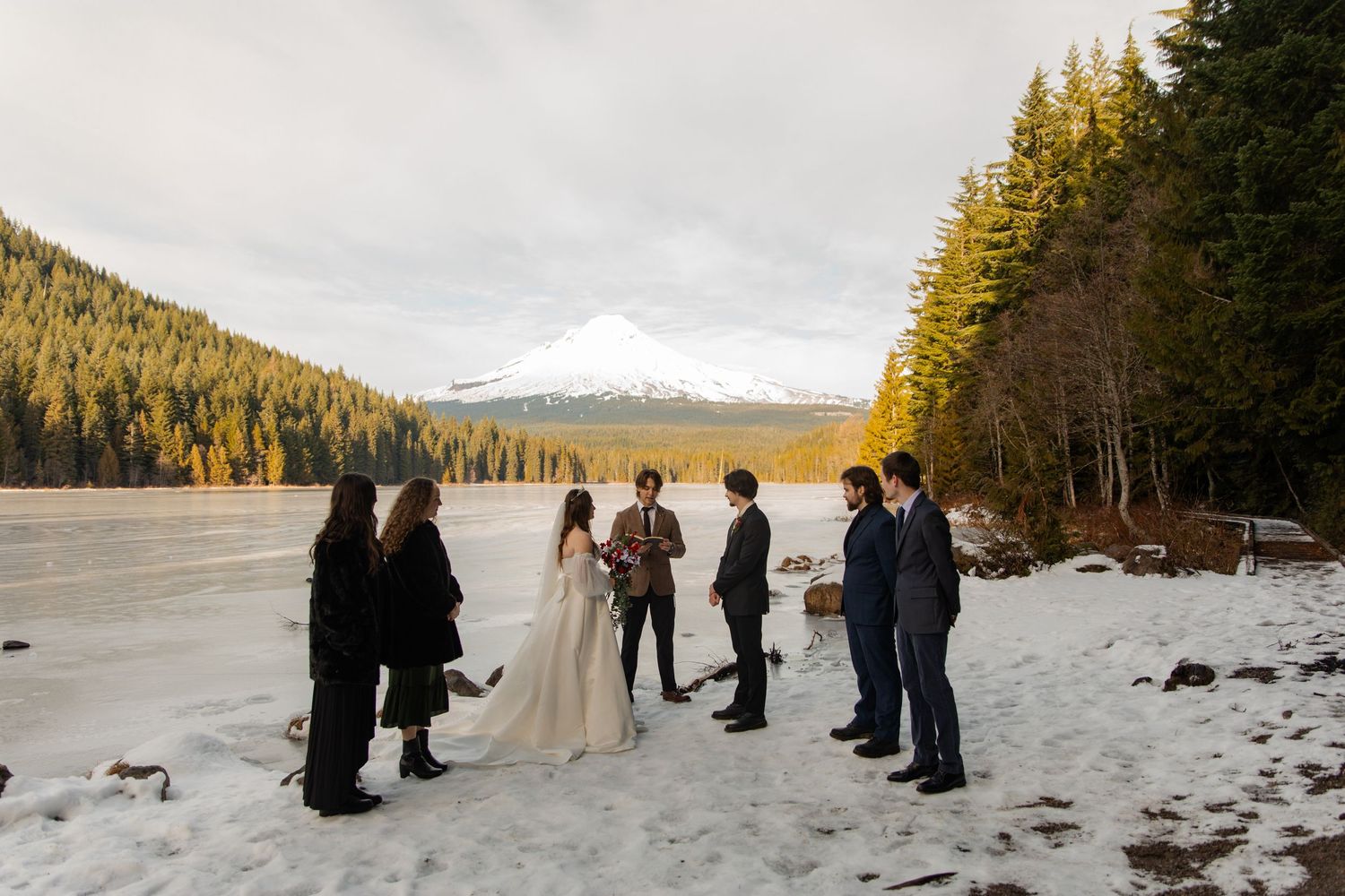 Small wedding ceremony gathering on a frozen lake surrounded by snow-capped mountains.