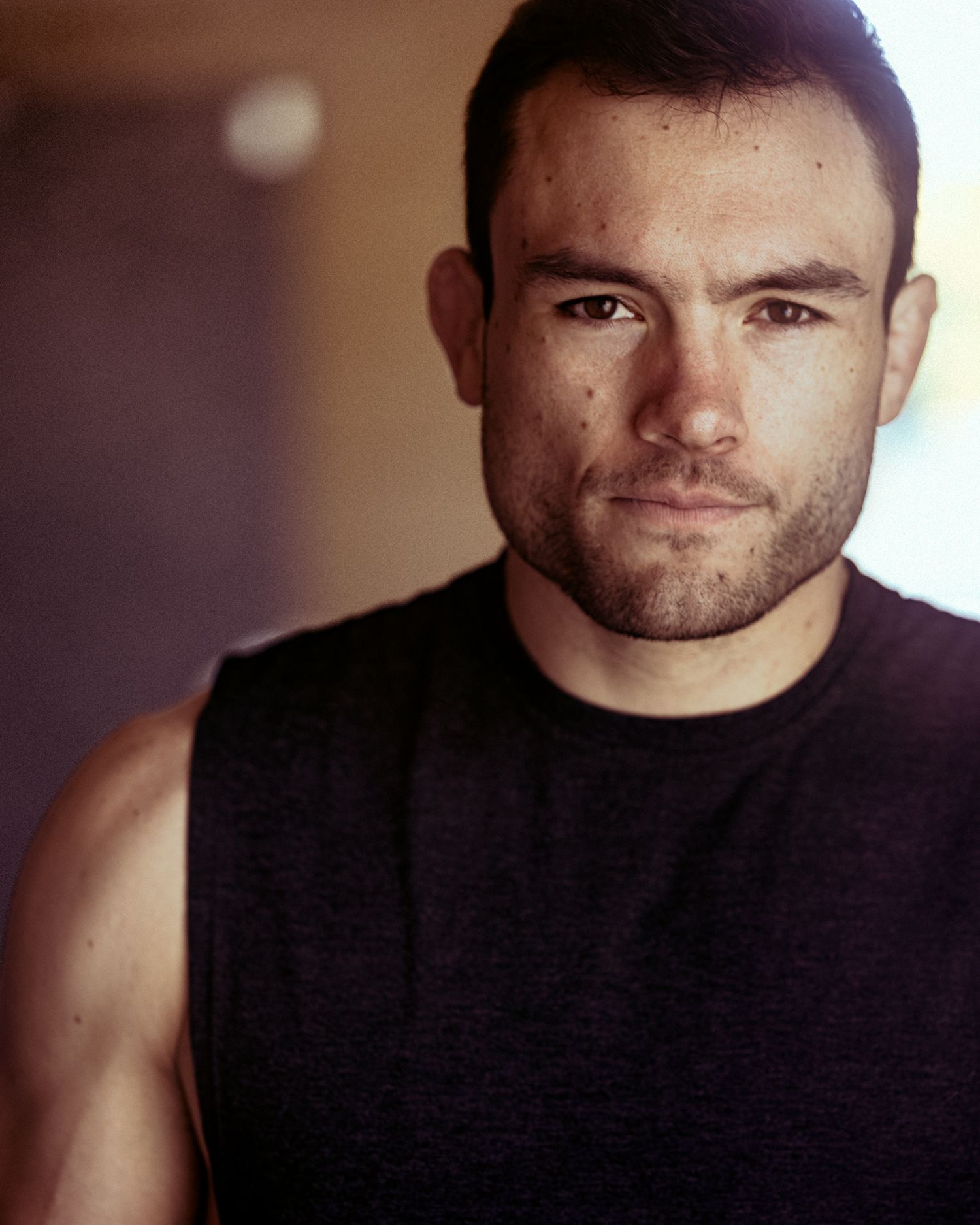 Athletic man in black sleeveless shirt poses for portrait with dramatic lighting.