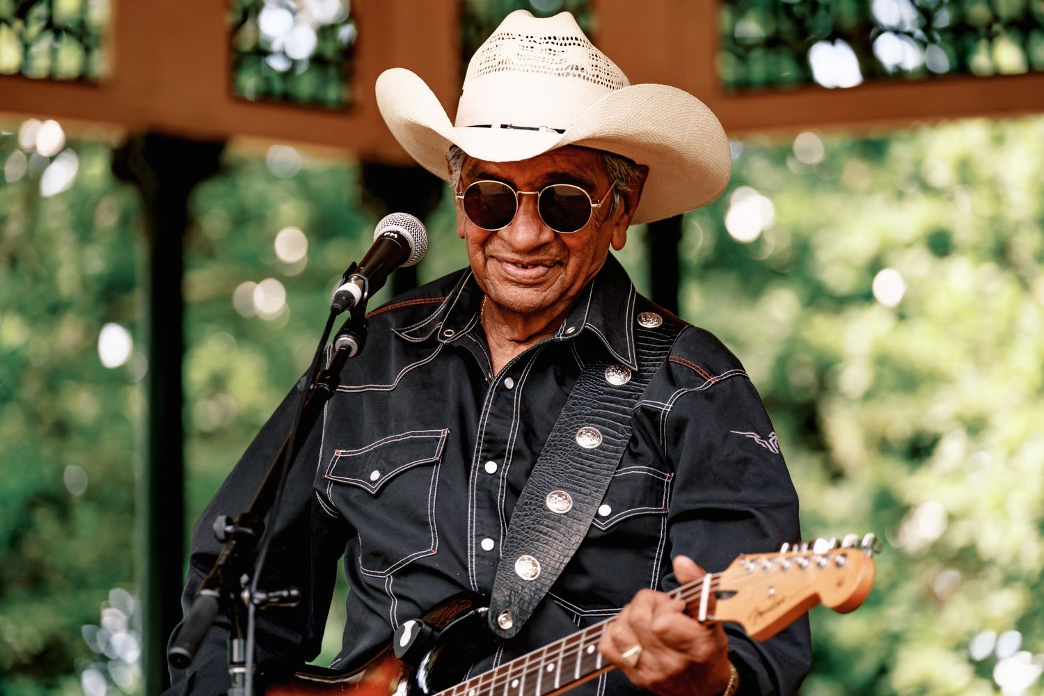 Musicians performing on stage wearing cowboy hats and playing guitars at an outdoor venue.