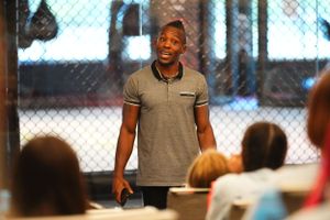 A speaker in a grey polo shirt addresses an audience during an engaging presentation in an indoor venue.