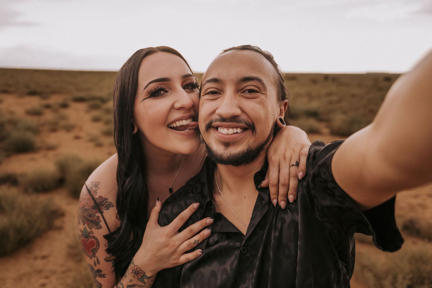 A couple takes a smiling selfie together in the desert with a New Mexico desert landscape behind them. LGBT wedding photographer Albuquerque