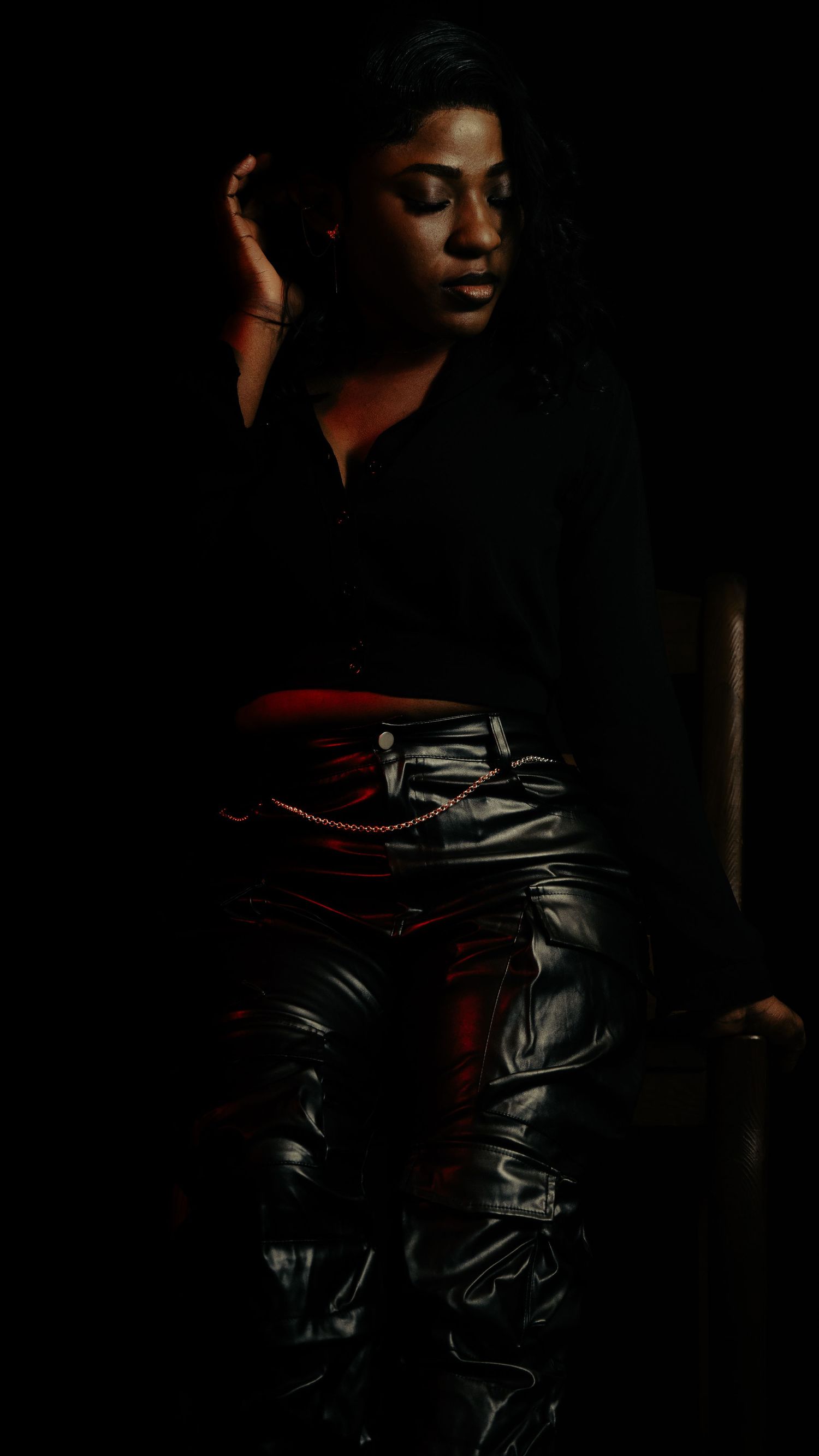 Dramatic dark portrait showcasing shiny leather pants in moody lighting against black background.