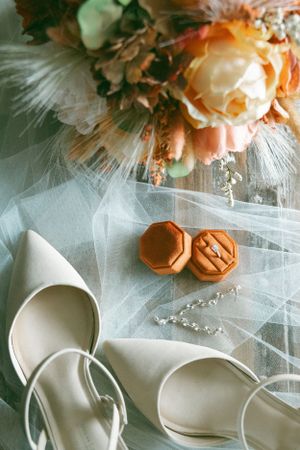 Wedding accessories including peach roses, white tulle fabric, and orange ring boxes arranged on a delicate surface.