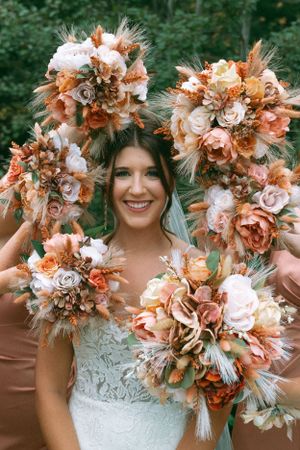 Beautiful autumn wedding bouquets featuring coral roses, white flowers and feathers in rustic bohemian style.