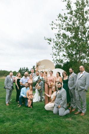 Wedding party poses together on grass lawn with overcast sky and trees in background.