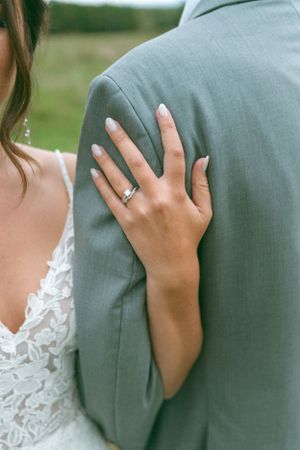 Close up of bride's hand with wedding ring resting on groom's gray suit jacket.
