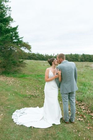 Couple in wedding attire sharing an intimate moment in a serene meadow with evergreen trees.