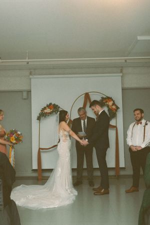 A wedding ceremony takes place under a floral arch with a long train wedding dress and officiant.