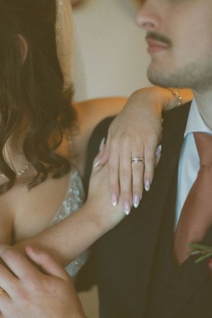 Close-up of a bride's hand with engagement ring resting on groom's suit jacket.