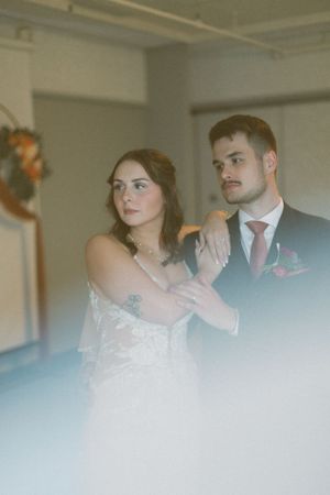 A dreamy soft-focus wedding portrait showing a couple in formal attire with white dress and black suit against a light interior.