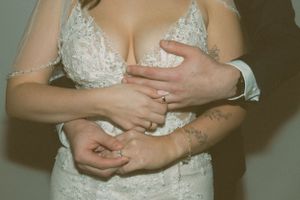 Close-up detail of hands resting on a white lace wedding dress with delicate embellishments.