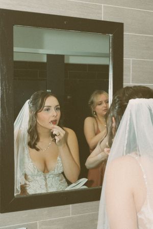 Wedding party getting ready with bride applying lipstick in front of bathroom mirror.