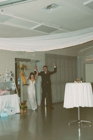 Wedding couple makes grand entrance at reception with arms raised in celebration.