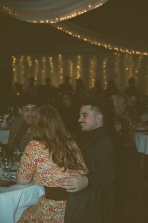 Wedding reception guests enjoying themselves under warm string light decorations.