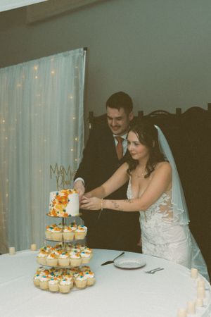 A wedding couple cuts their tiered cupcake display together at their reception.