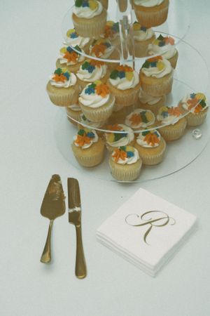 Elegant cupcake display on tiered stand with gold serving utensils and monogrammed napkins at a formal event.