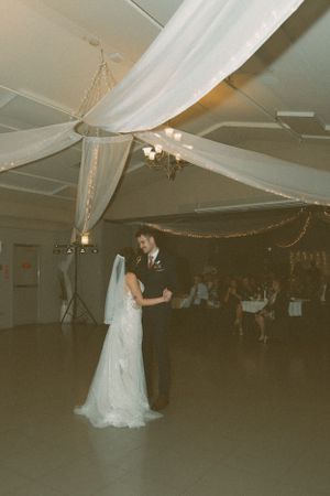 Wedding reception venue decorated with white fabric draping and twinkling lights on ceiling.