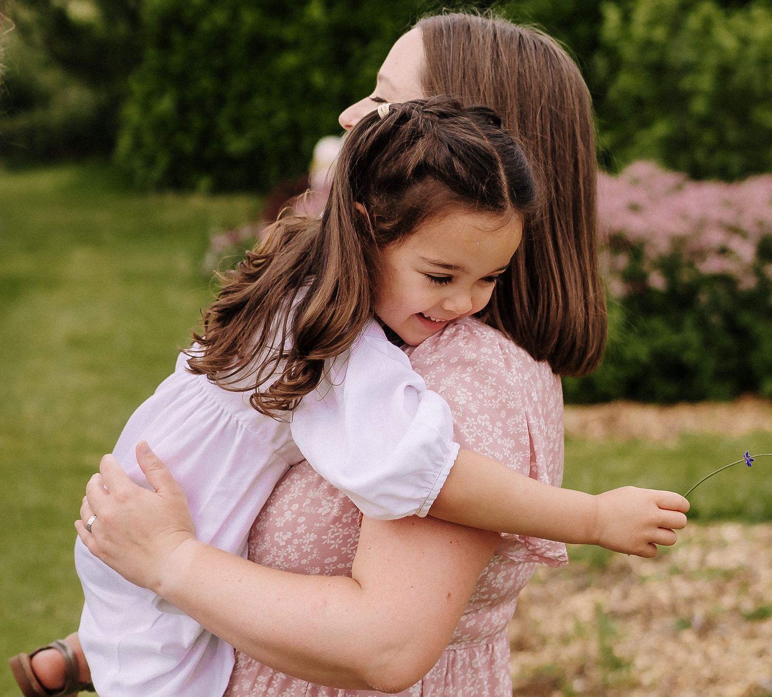 A tender embrace shared between parent and child in a garden with pink flowers in the background.