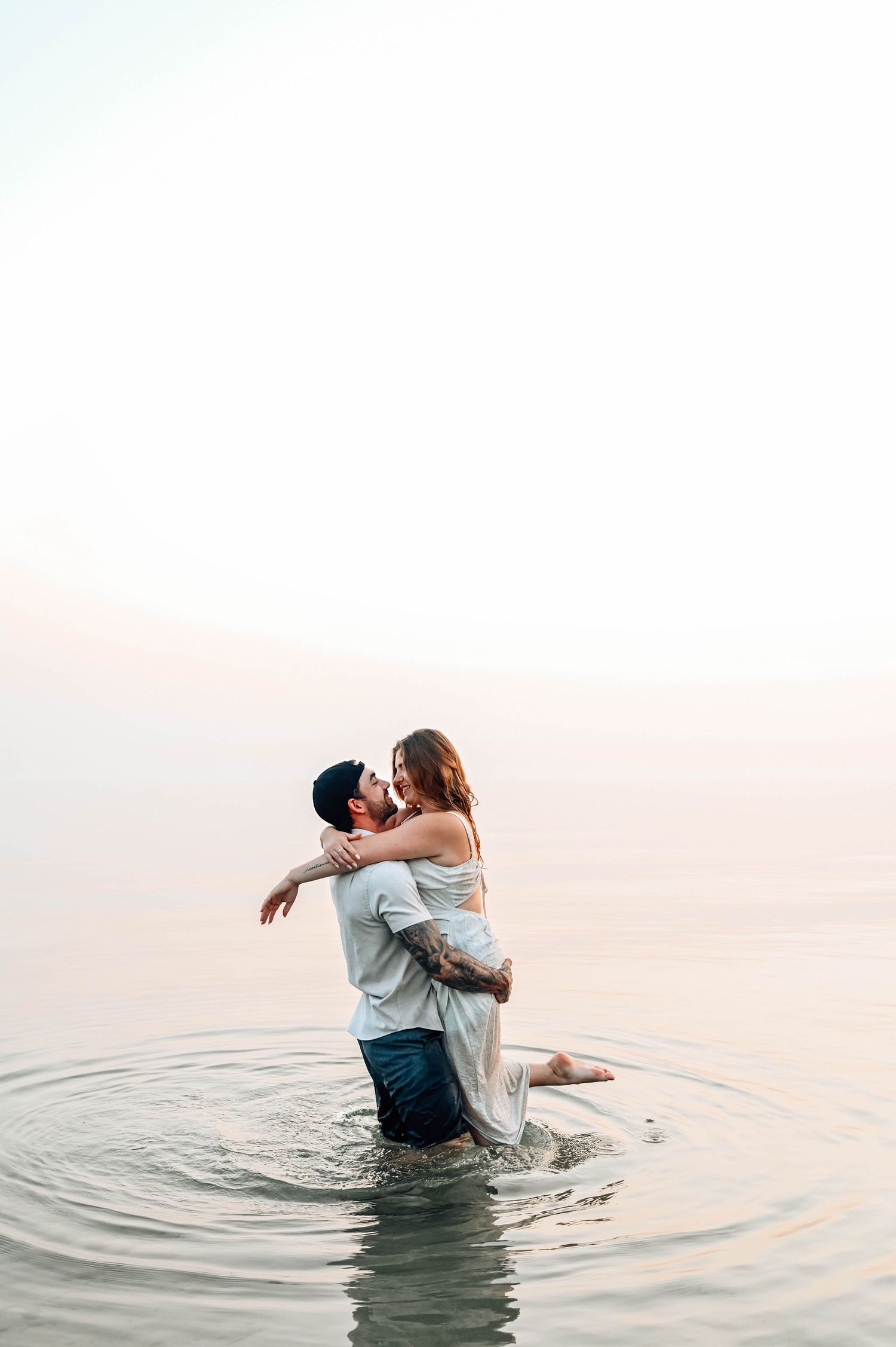 Couple embracing in calm water during sunset creating ripples around them as they hold each other.