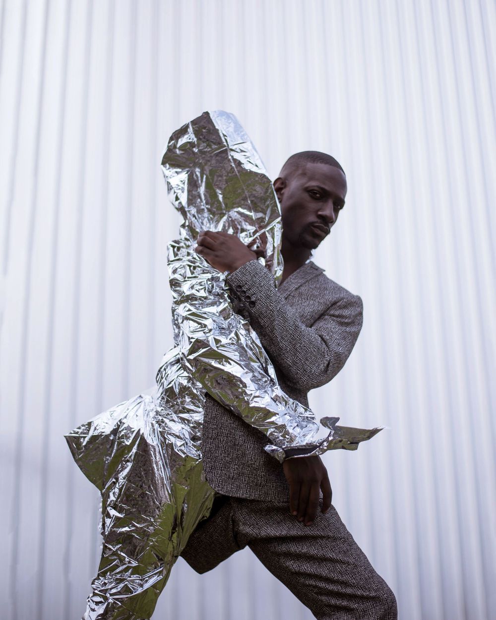 Artistic photo of person in gray suit posing with metallic silver foil material against white background.