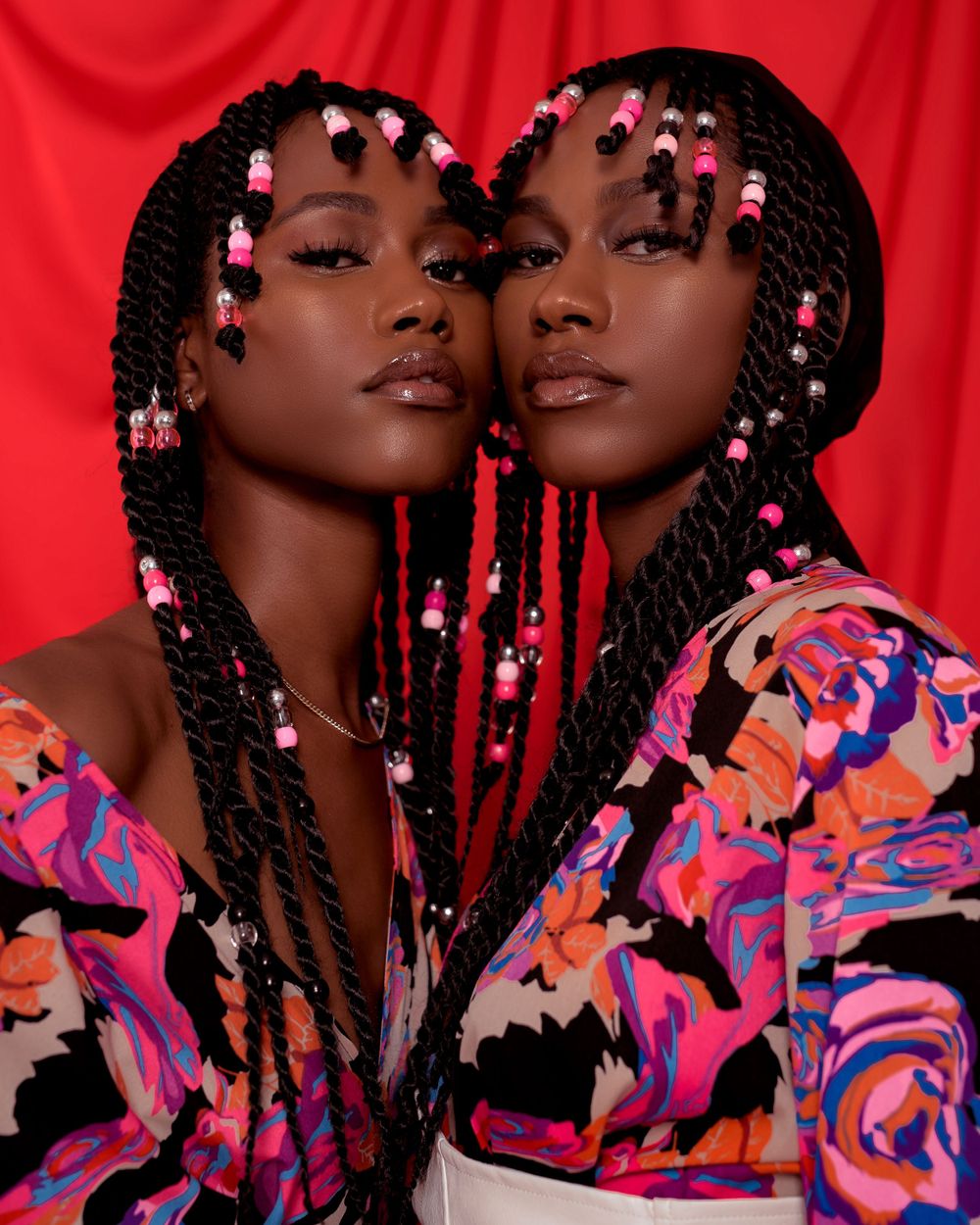 Beauty portrait with decorative braids and colorful floral print clothing against red background.
