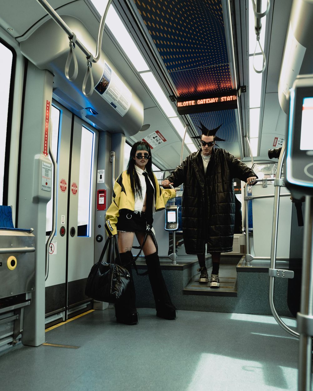 Fashion editorial shot of two people posing in stylish outfits inside modern train car.