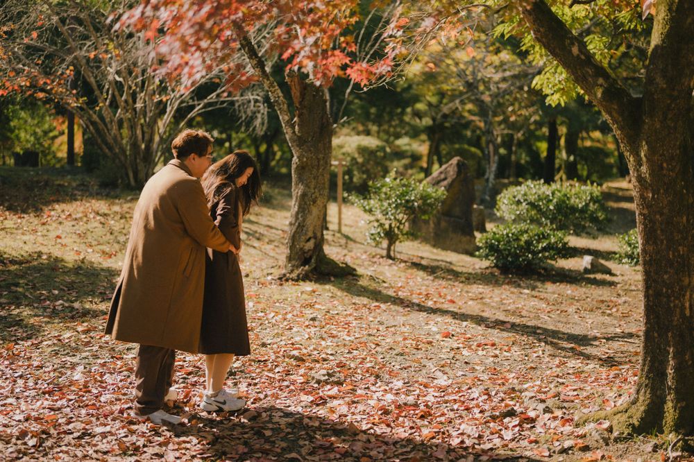 Couple sharing a kiss surrounded by brilliant red and orange autumn foliage in a peaceful Japanese garden.