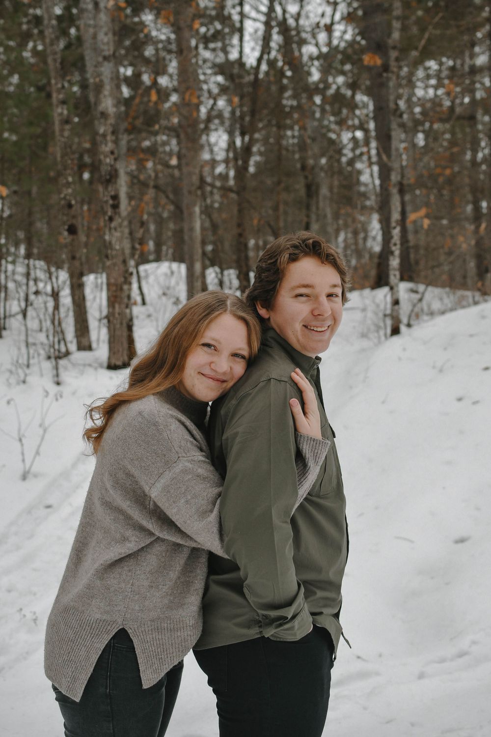 A couple shares a sweet moment while posing together on a snowy winter trail surrounded by bare trees.