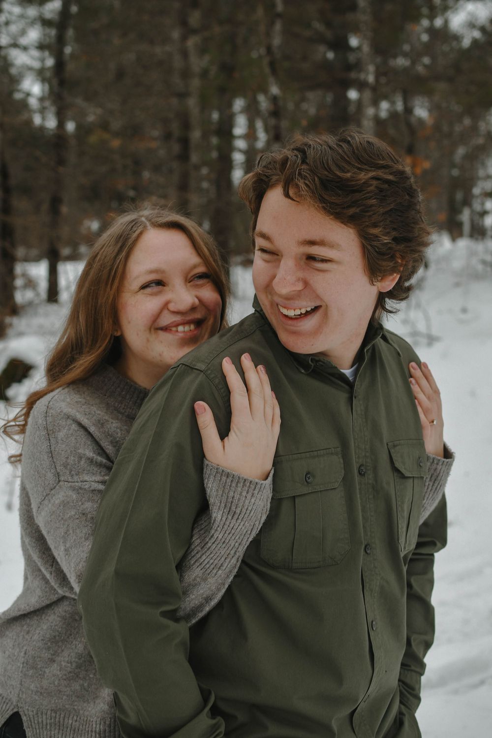 A happy couple embraces while sharing a candid moment together in a snowy winter forest setting.