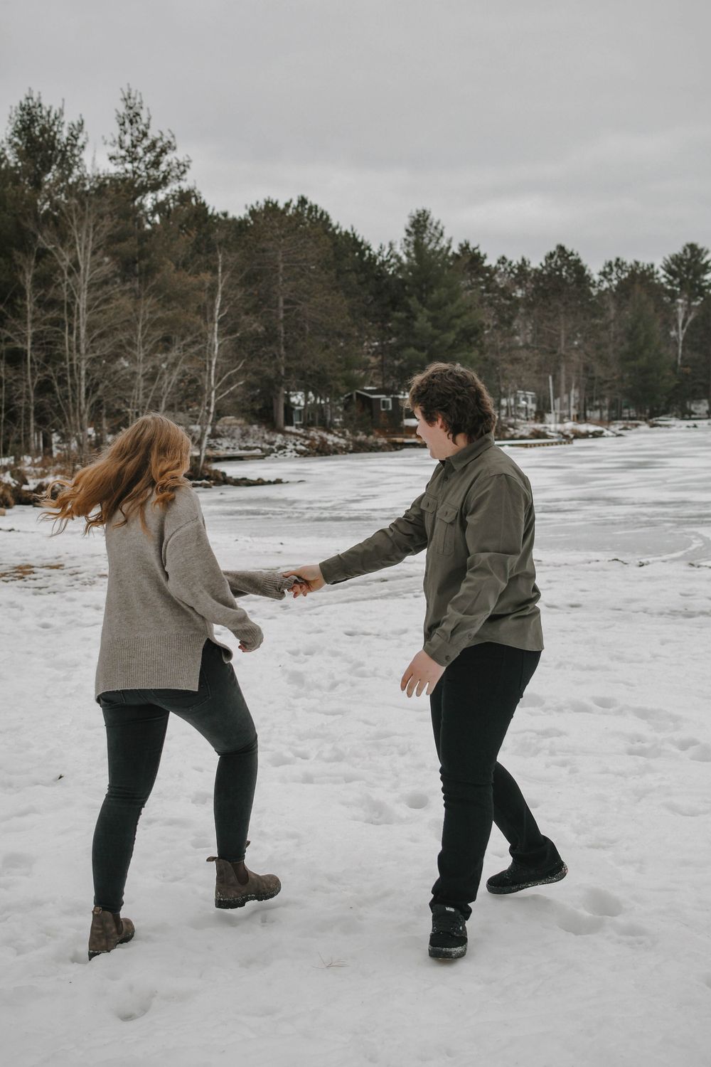 Couple dancing together on a frozen lake with snow-covered pine forest in the background during winter.