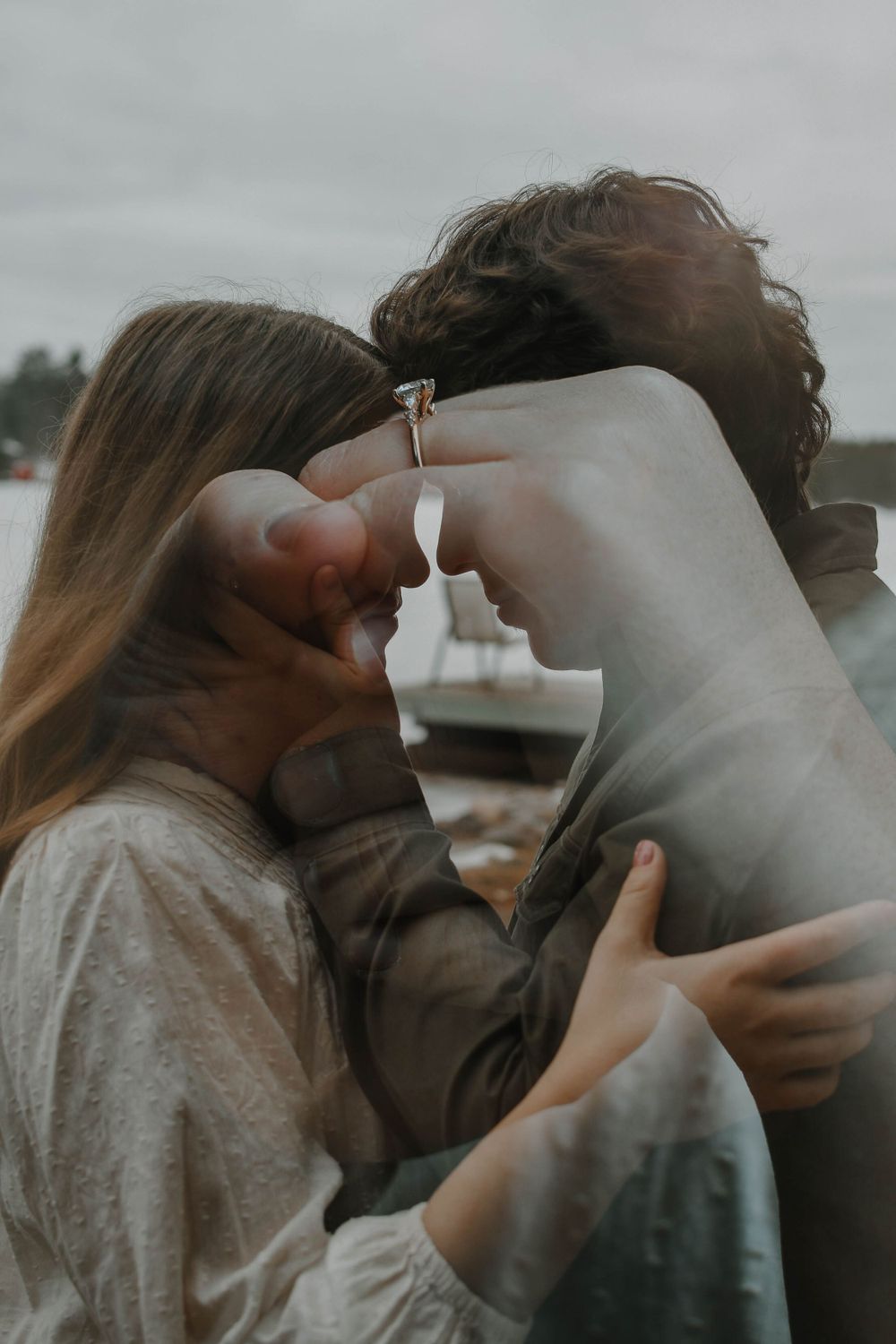 An intimate couple share a tender embrace and kiss in moody overcast lighting outdoors.