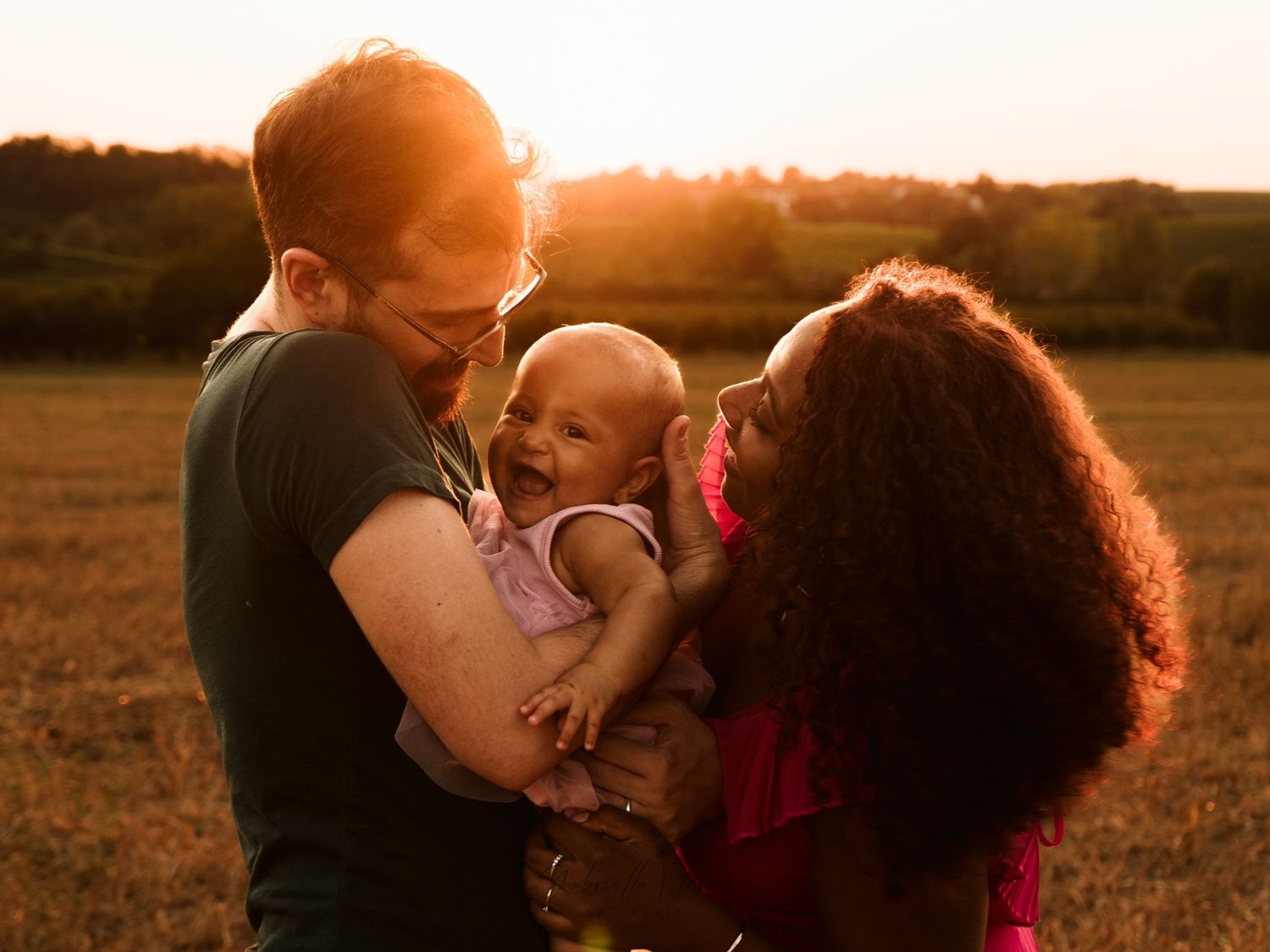 Famiglia romantica che si abbraccia durante il servizio fotografico al tramonto con una calda illuminazione dorata.