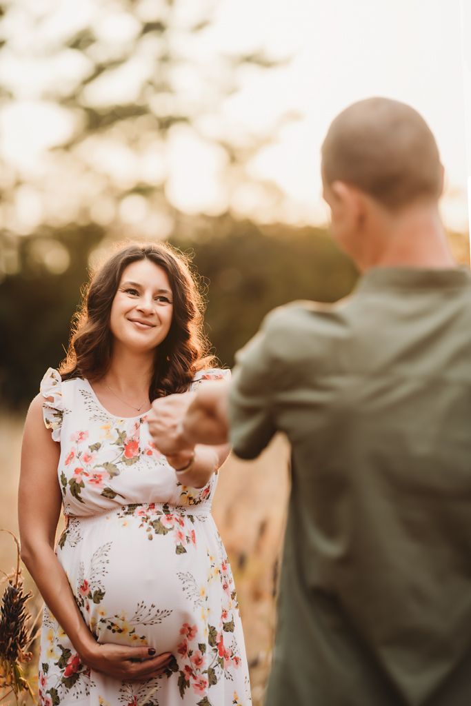 A couple shares a joyful moment during their maternity photoshoot in a golden field.