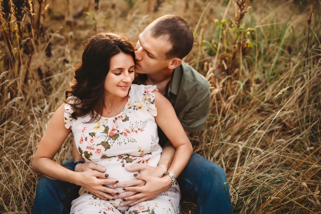 An intimate maternity portrait of a couple sitting in tall grass during sunset.