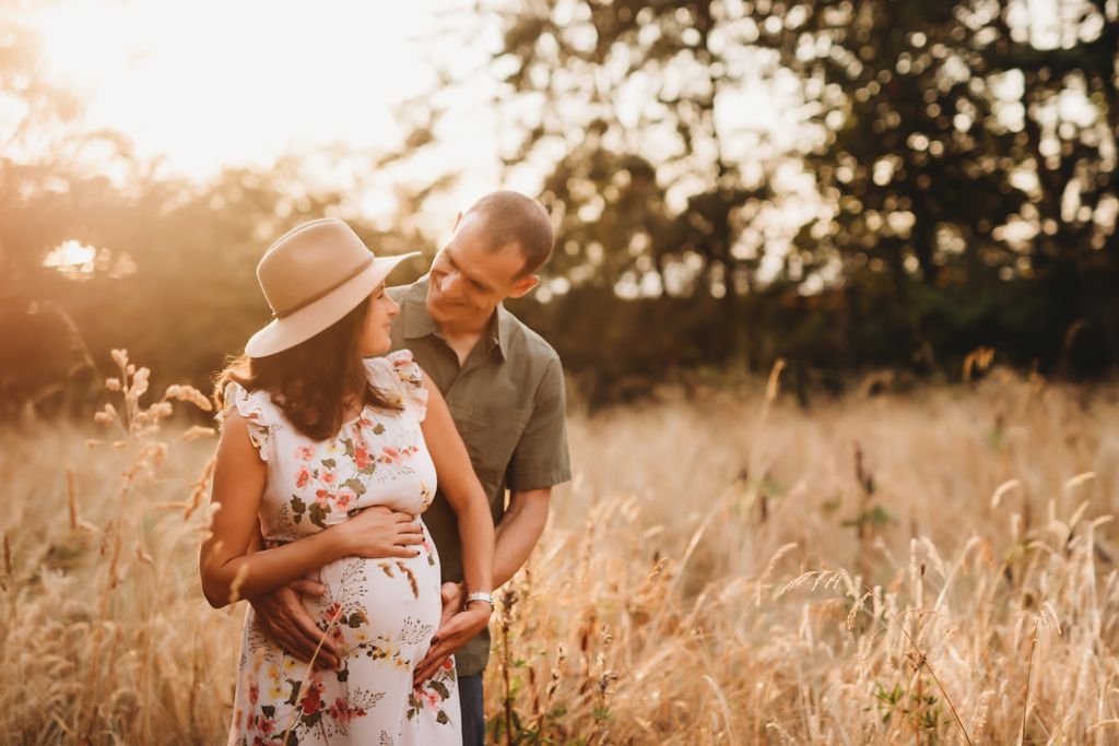 A maternity photoshoot featuring a couple embracing in a golden wheat field at sunset.