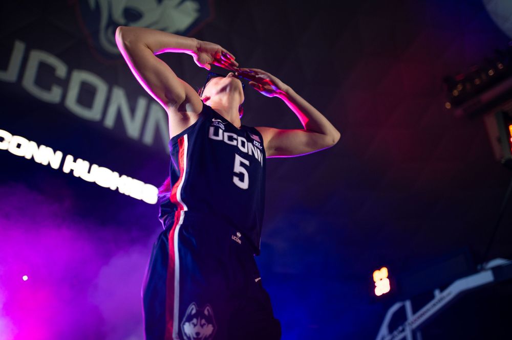 Basketball player in UConn jersey number 5 gestures during dramatic pre-game introduction with colorful lighting.